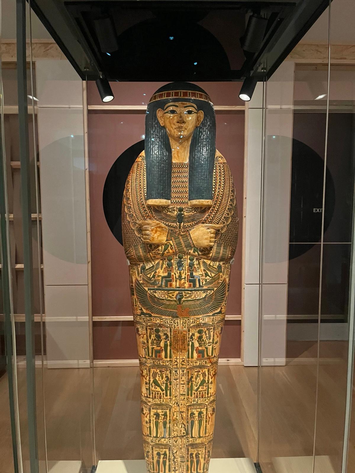 An Egyptian coffin with gilded face and arms crossed over chest.